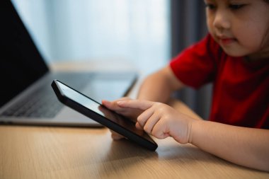 Cep telefonu ekranını kullanan ve dokunan Asyalı bir kız çocuğu. Bebek gülümsemesi cep telefonu kullanmak için komik bir zaman. Çok fazla ekran zamanı. Oturma odasında televizyon seyreden tatlı bir kız, internet bağımlılığı..