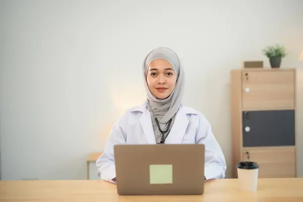 Muslim islam Asian doctor man wearing hijab and stethoscope working with laptop computer. Female doctor work at home office hospital. Health hospital concept.