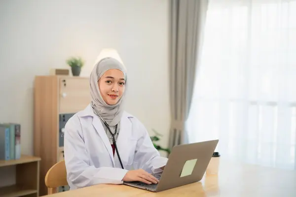 Muslim islam Asian doctor man wearing hijab and stethoscope working with laptop computer. Female doctor work at home office hospital. Health hospital concept.