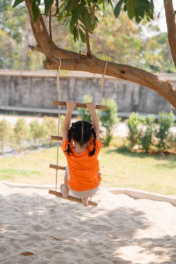 Arkadan bak. Genç Kız Halat Merdiveni 'nde Oynuyor. Turuncu tişörtlü küçük bir kız çocuk parkında ip merdivene tırmanıyor, konsantrasyonuyla. Bebek kız çocuk aktivite konsepti.