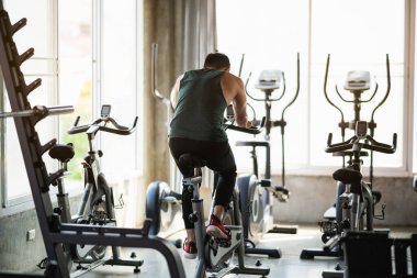 Arkadan bak. Spor salonunda bisiklet üzerinde egzersiz yapan Asyalı sporcu, kardiyo azmi onu sağlıklı kılıyor. Egzersiz bisikleti sporu konsepti.