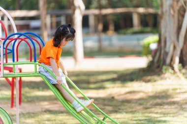 Cute asian girl smile play on school or kindergarten yard or playground. Healthy summer activity for children. Little asian girl climbing outdoors at playground. Child playing on outdoor playground.