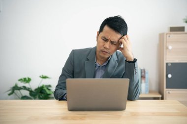 Üzücü derecede ciddi Asyalı iş adamı stresli bir depresyon yaşıyor ve ofis masasında dizüstü bilgisayarla çalışıyor. Yüzünde bir hüsran ifadesiyle ekrana bakıyor..