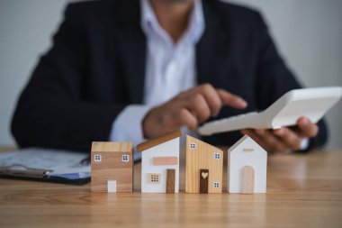 Ahşap Ev Modelleri Profesyonel Değerlendirme. Hesap makineli bir iş adamı ahşap ev modellerini analiz ediyor, gayrimenkul değerlendirmesi kavramını kullanıyor. Konut kredisi veya faiz kavramı.