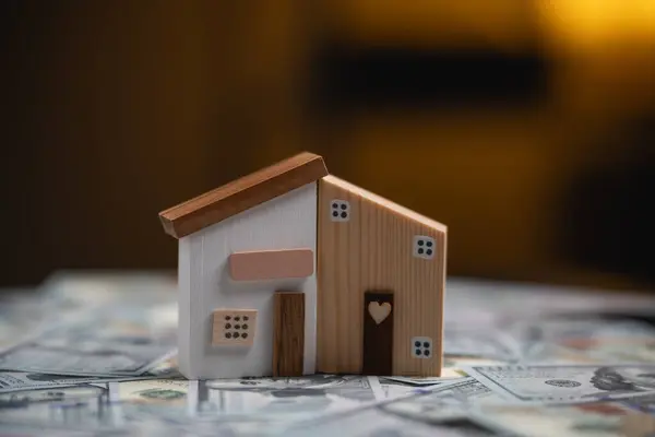 Charming Wooden House Model on Cash Background. A quaint wooden house model stands on a background of scattered US dollar bills. Finance home loan or interest concept.