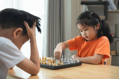 İki çocuk satranç oynuyor. Biri beyaz gömlek giyiyor ve diğeri turuncu gömlek giyiyor.