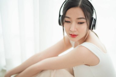 Uzun siyah saçlı, beyaz kolsuz tişörtlü, kulaklık takan, parlak bir odada müziğin keyfini çıkaran güzel bir genç kadın. Huzurlu ve mutlu görünüyor. İnce bir gülümseme ve hafif bir ışıkla..