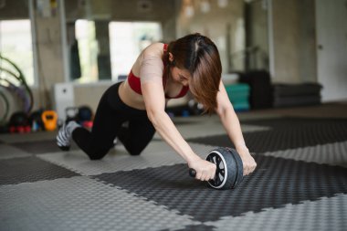 Asyalı kadın paspasın üstünde egzersiz yapıyor. Elinde bir fitness topu tutuyor ve mekik çekiyor. Spor salonu kavramları.