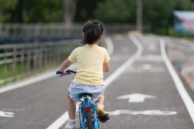 Asyalı bir bebeğin park bahçesinde bisiklet sürmeyi öğrenmesi. Çocuk bisiklet pratiği için eğitim konsepti, bebek sporları konsepti.