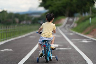 Asyalı bir bebeğin park bahçesinde bisiklet sürmeyi öğrenmesi. Çocuk bisiklet pratiği için eğitim konsepti, bebek sporları konsepti.