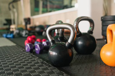 Siyah ve turuncu bir çaydanlık siyah bir mindere oturur. Mor ve mavi bir kettlebell 'in yanında.