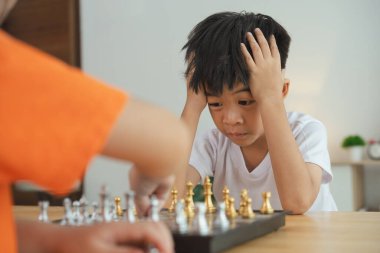 İki çocuk satranç oynuyor. Biri beyaz gömlek giyiyor ve diğeri turuncu gömlek giyiyor.