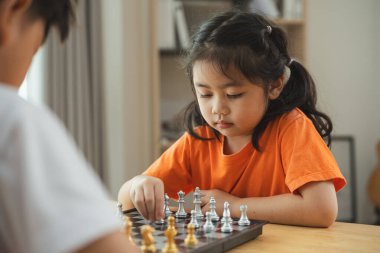 İki çocuk satranç oynuyor. Biri beyaz gömlek giyiyor ve diğeri turuncu gömlek giyiyor.