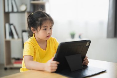 Asyalı genç kız önünde bir tabletle bir masada oturuyor. Yüzünde ciddi bir ifadeyle ekrana bakıyor.