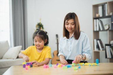 Asyalı bir kadın ve bir çocuk bloklarla oynuyorlar. Kadın, çocuğun kule yapmasına yardım ediyor.