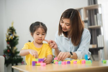 Asyalı bir kadın ve bir çocuk bloklarla oynuyorlar. Kadın, çocuğun kule yapmasına yardım ediyor.