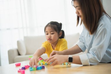 Asyalı bir kadın ve bir çocuk bloklarla oynuyorlar. Kadın, çocuğun kule yapmasına yardım ediyor.