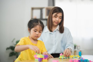 Asyalı bir kadın ve bir çocuk bloklarla oynuyorlar. Kadın, çocuğun kule yapmasına yardım ediyor.