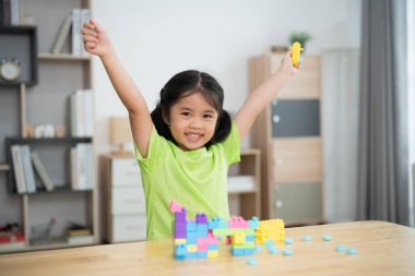 Genç bir kız önünde renkli bir yığın blokla bir masada oturuyordu. Gülümsüyor ve eğleniyor.
