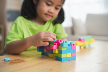 Genç bir kız ahşap bir masada renkli bloklarla oynuyor. O, bloklardan bir kule inşa ederken gülümsüyor. Bloklar farklı şekil ve boyutlarda.