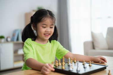 Genç bir kız tahta ve taşlarla satranç oynuyor. Gülümsüyor ve eğleniyor.