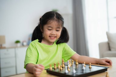 Genç bir kız tahta ve taşlarla satranç oynuyor. Gülümsüyor ve eğleniyor.