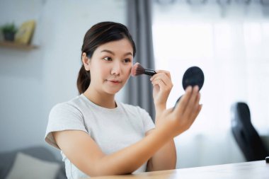 Asyalı kadın aynanın önünde makyaj yapıyor. Makyaj yapmak için fırça kullanıyor.