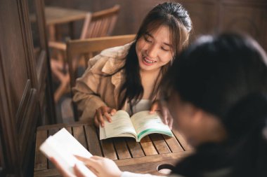 İki kadın bir masada oturuyor, biri kitap okuyor. Olay yeri dostane ve rahat.
