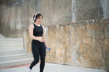 Genç bir kadın şehir merdivenlerinde spor yaparken şık bir giysi ve kulaklık takarak müzik ve hidrasyonun keyfini çıkarıyor..