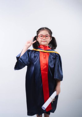 Mezuniyet elbisesi ve gözlük takan neşeli genç bir kız diplomasını tutarken bir barış işareti yapıyor ve akademik başarının sevincini yakalıyor..