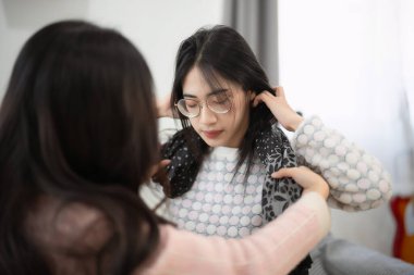 Biri diğerinin saçını şekillendirirken, iki genç kadın, evdeki arkadaşlığı ve paylaşılan anları yansıtıyor.