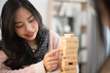Tahta bloklarla oynayan genç bir kadın, gülümsüyor, parmaklarına odaklanıyor, kapalı mekanlarda rahat bir ortam kuruyor, rahatlıyor ve eğleniyor, arkadaşça bir yarışmaya katılıyor.
