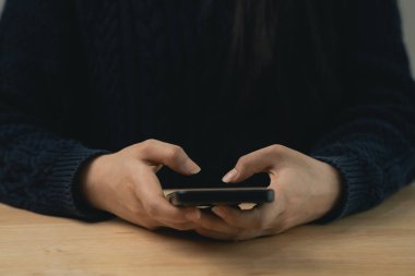 Bir insanın ellerinin akıllı bir telefonu tutarken yakın plan görüntüsü, teknolojiyle samimi bir etkileşim sergilerken ahşap bir masada rahat bir şekilde otururken.