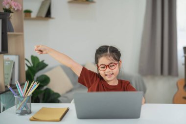 Mutlu çocuk evde bilgisayarla çalışırken başarıyı kutluyor, neşeli ve misafirperver bir ortamda sevinç ve coşku gösteriyor.