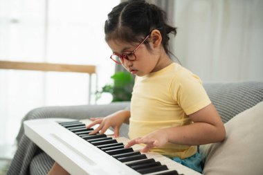 Sarı tişörtlü genç kız evde klavye çalıyor. Odaklanma ve konsantrasyonla, rahat bir koltukta otururken müzik yeteneğini ve yaratıcılığını keşfediyor.