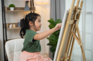 Mutlu genç kız evde yaratıcı resim yapmaktan zevk alıyor, parlak ve neşeli kapalı alanda tuvaller üzerinde çalışıyor, çocuklar için sanat ve eğlence aktiviteleri yapıyor.