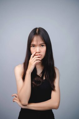 Uzun siyah saçları ve doğal ifadesi olan düşünceli genç bir kadın. Gri bir arka plana karşı poz veriyor. Duygusal tefekkür ve içgözlem sergiliyor..