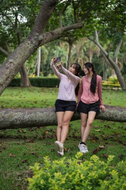 Etrafı Ağaçlar ve Doğal Güzelliklerle çevrili Yeşillik Parkı 'nda Selfie Çeken İki Genç Kadın Birlikte Açık Hava Eğlencesinin keyfini çıkarıyorlar.