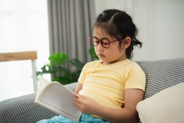 Gözlüklü Genç Kız Parlak ve Modern Oturma Odasında Doğal Işık ve Yeşil Bitkilerle Konforlu Bir Koltukta Kitap Okuyor