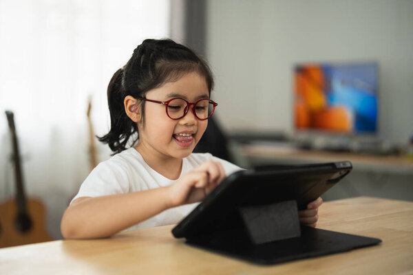 Cheerful Asian girl with glasses engaging with tablet computer at home in cozy environment, learning, and enjoying digital technology in modern setting