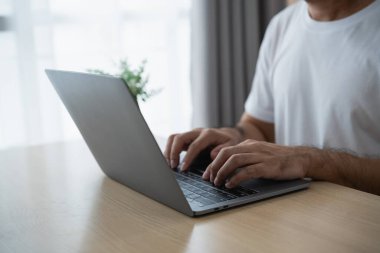 Parlak, minimalist bir odada dizüstü bilgisayarla yazı yazan biri. Klavye üzerinde çalışan ellere odaklanma, evden çalışma ortamında verimlilik ve konforu artırma.