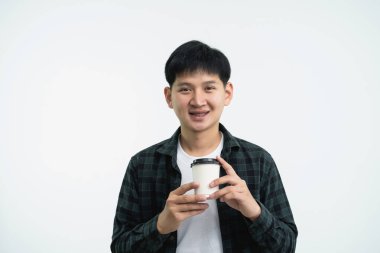 Minimalist bir stüdyo ortamında elinde kahve fincanı tutan genç bir adam, günlük kıyafetler giyiyor ve arka planda hafif bir poz veriyor.