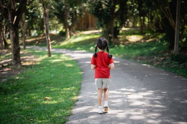 Genç bir çocuk ağaçlarla çevrili sakin bir parkta yürüyor, güneşli bir günde doğada huzurlu bir anın tadını çıkarıyor.