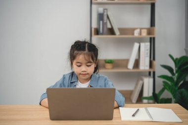 Evde dizüstü bilgisayarla çalışan odaklanmış genç bir kız. Etrafı kitaplıklarla çevrili, rahat ve modern bir çalışma alanı ortamında..