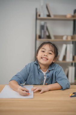 Gülümseyen genç bir kız evde yaratıcı çizim yapıyor, rahat bir ortamda öğrenme ve sanatsal ifade sergiliyor.