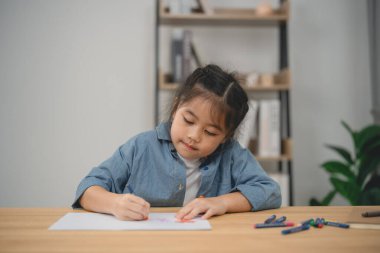 Evde renkli boya kalemleriyle yaratıcı çizimler yapan genç bir kız ev ortamında odak ve hayal gücü sergiliyor.