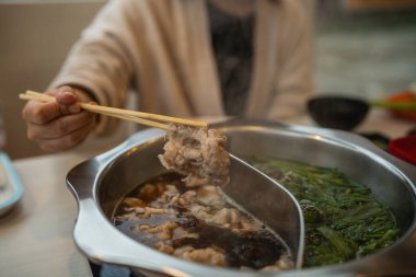 Sıcak bir yemek sahnesinde sıcak bir atmosferde yükselen yemek çubuklarının ve buharın altını çizen lezzetli çorbaya batırılmış taze malzemelerle dolu sıcak bir tencere var..