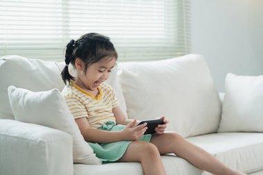 Genç Kız, Parlak Oturma Odası 'nda rahat bir şekilde otururken ve camdan içeri ışık girerken akıllı telefonuyla nişanlandı.