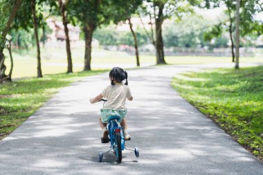 Genç bir çocuk huzur parkında üç tekerlekli bisiklet sürüyor ağaçlarla çevrili, güneş ışığı yaprakların arasından süzülüyor, neşeli açık hava deneyimi, çocukluk macerası