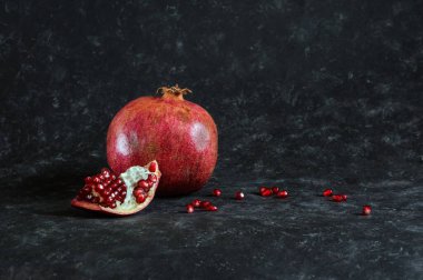 Juicy pomegranate and a piece of fruit with red seeds on a shabby dark background with copy space. natural light, selective focus